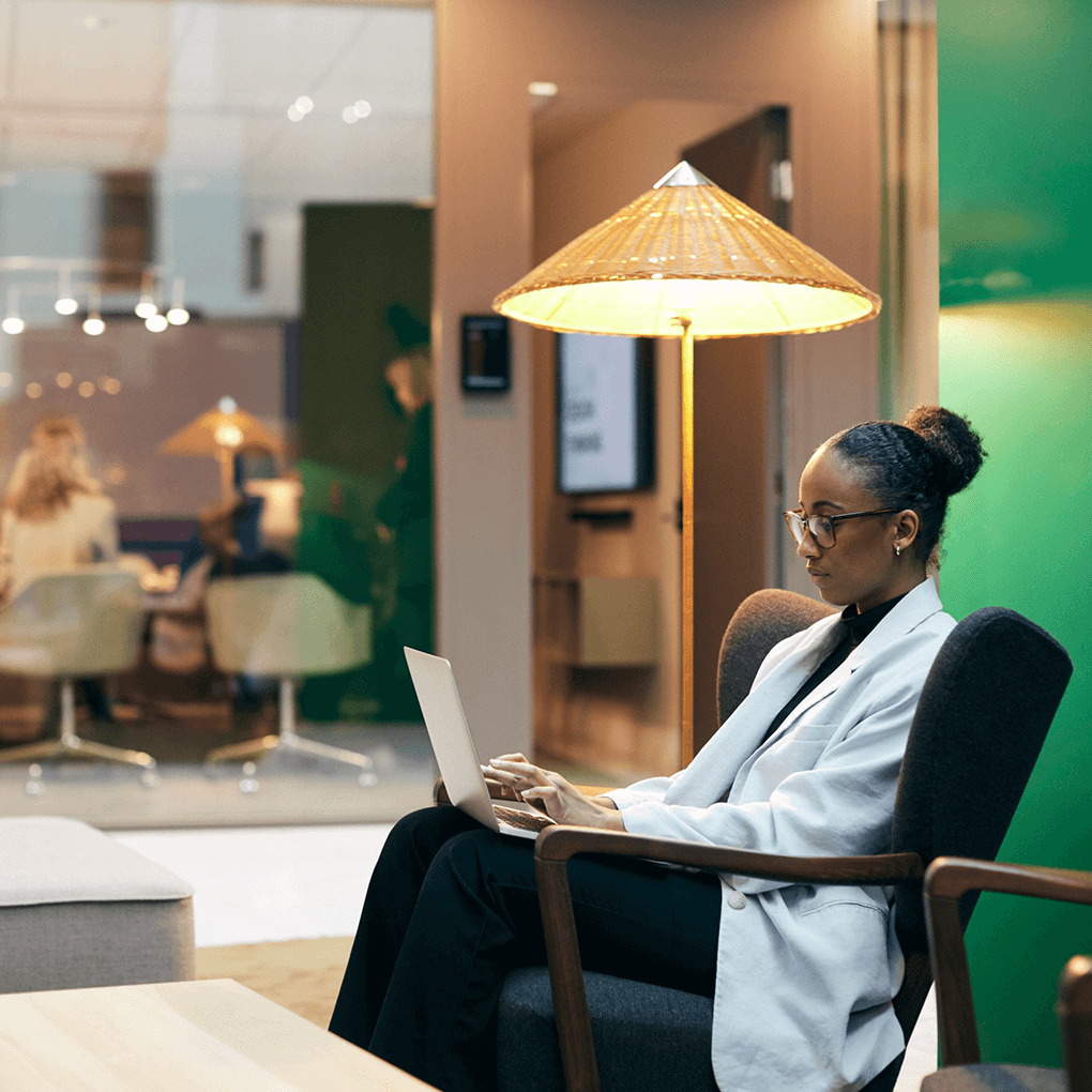 A professional woman working on her laptop in a modern office lounge, utilizing a digital contract generator to streamline her document creation process.