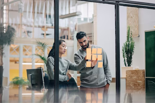 Two people looking at sticky notes on a glass wall